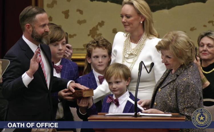 ELECTED TX SPEAKER State Rep. Dustin Burrows was administered the oath of office as Speaker of the Texas House by Secretary of State Jane Nelson (right) during opening day ceremonies on the House floor on Tuesday, Jan. 14, 2025, as Burrows’wife, Elisabeth (in white dress), and children look on. | BOB DAEMMRICH FOR THE TEXAS TRIBUNE